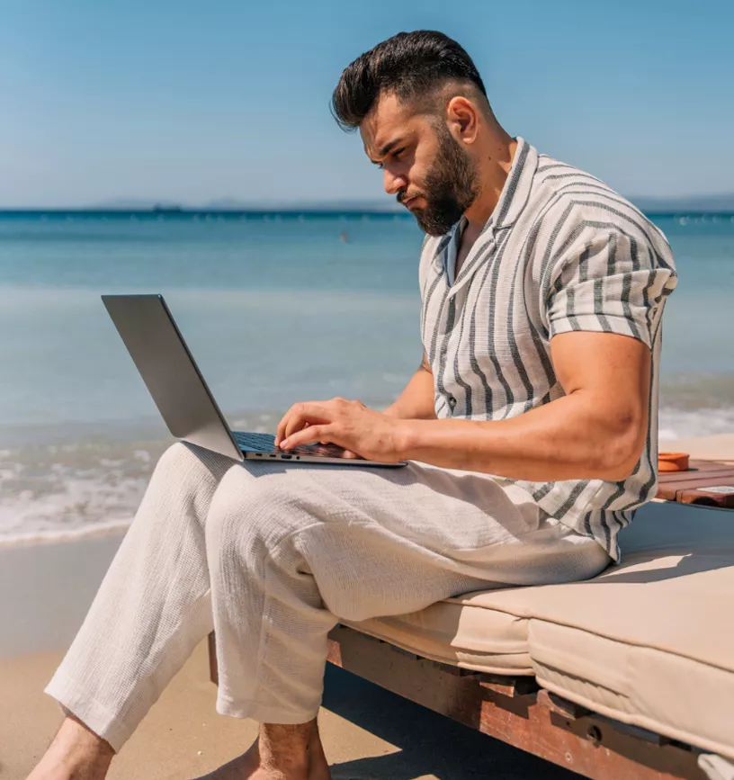 Hombre trabajando con su laptop sentado frente al mar en la playa